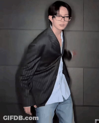 Man In Glasses And Jacket Standing In Front Of Wall GIF