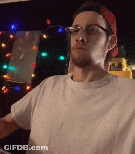 Man In Glasses And Red Hat Standing In Front Of Christmas Tree GIF