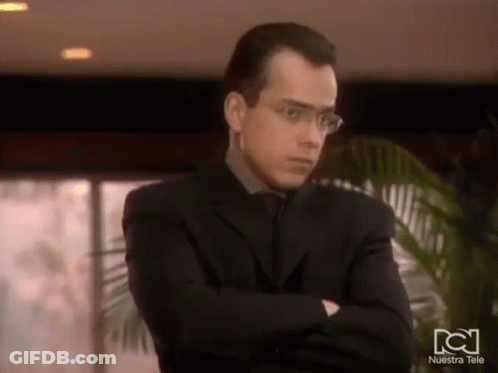 Man In Glasses And Suit With Arms Crossed In Front Of Nuestra Tele Logo GIF