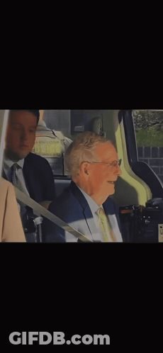 Man In Glasses And Tan Coat Sitting In Blue Chair GIF