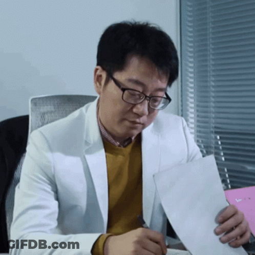 Man In Glasses And White Jacket Holding Paper At Desk GIF
