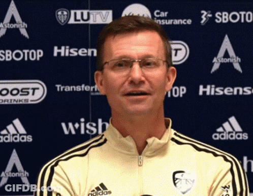 Man In Glasses And Yellow Adidas Shirt In Front Of Ad Wall For Hisen Sbotop And Wish GIF