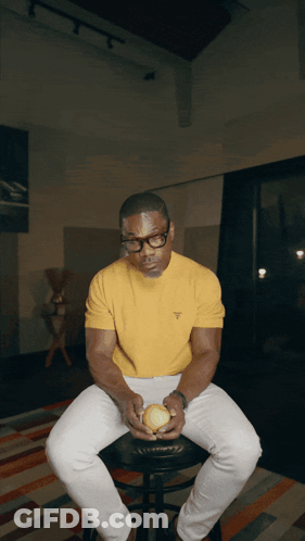 Man In Glasses And Yellow Shirt Holding Tennis Ball On Stool GIF