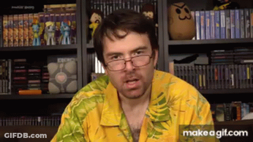 Man In Glasses And Yellow Shirt In Front Of Bookshelf Of Video Games GIF