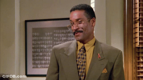 Man In Glasses And Yellow Shirt In Front Of Numbered Picture GIF