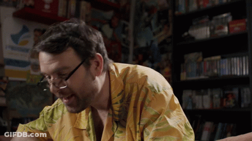 Man In Glasses And Yellow Shirt Sitting In Front Of PlayStation Sign GIF
