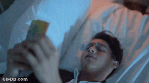 Man In Glasses Laying In Bed On Phone GIF