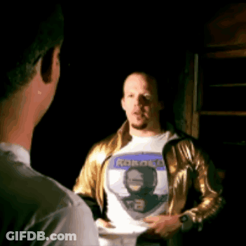 Man In Gold Jacket Talking To Man In Robot T-Shirt GIF