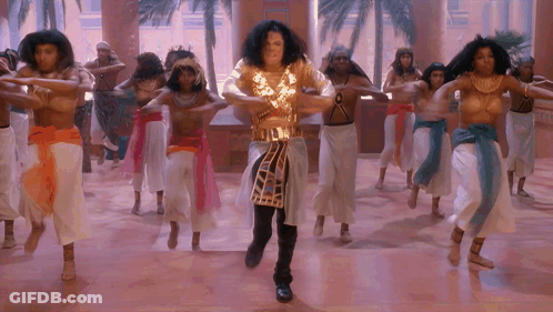 Man In Gold Outfit Dancing In Front Of Naked Women GIF