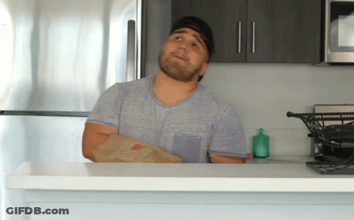 Man In Gray Shirt Holding Bag Of Food In Kitchen GIF