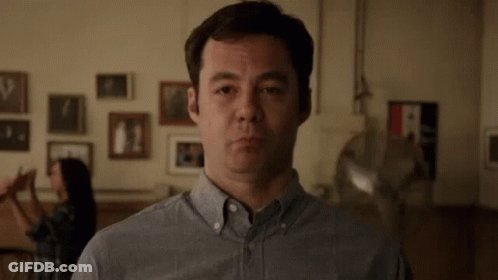 Man In Gray Shirt Making Funny Face With Woman Behind GIF