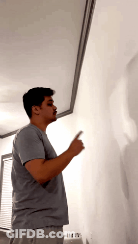 Man In Gray Shirt Pointing At White Wall GIF