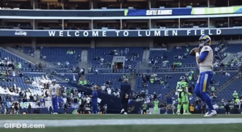 Man In Gray Shirt Talking To Man In Suit On Football Field GIF
