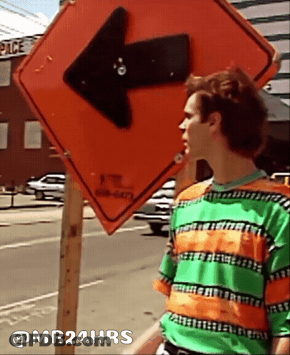 Man In Green And Orange Striped Shirt Beside Arrow Sign GIF