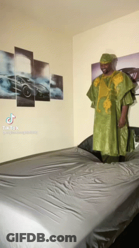 Man In Green Dress Standing On Bed With Cars Wall GIF