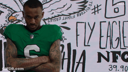 Man In Green Eagles Jersey In Front Of Fly Eagles Sign GIF