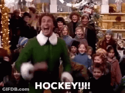 Man In Green Elf Costume Holding Hockey Stick GIF