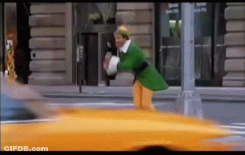 Man In Green Elf Costume Walking Next To Yellow Taxi GIF
