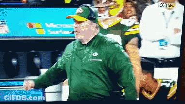 Man In Green Jacket And Hat In Front Of Fox NFL Sign GIF
