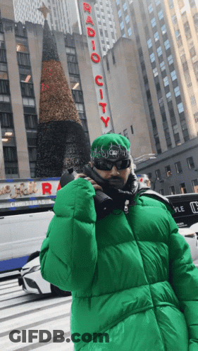 Man In Green Jacket In Front Of Radio City Building GIF