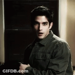 Man In Green Jacket Looking At Camera In Dark Room GIF