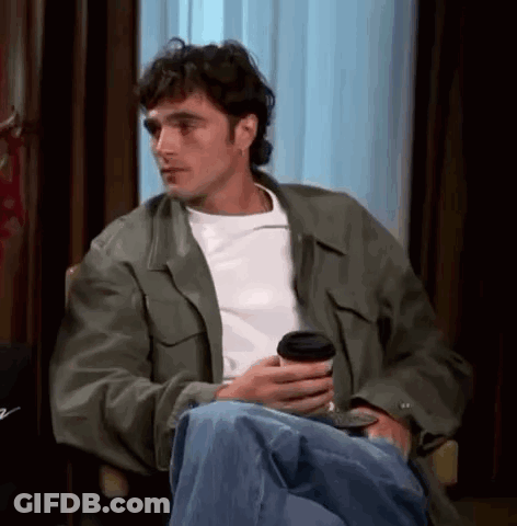 Man In Green Jacket Sitting In Chair Holding Coffee GIF