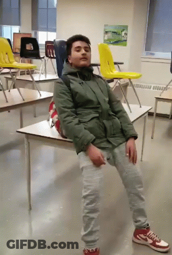 Man In Green Jacket Sitting On Desk In Classroom GIF