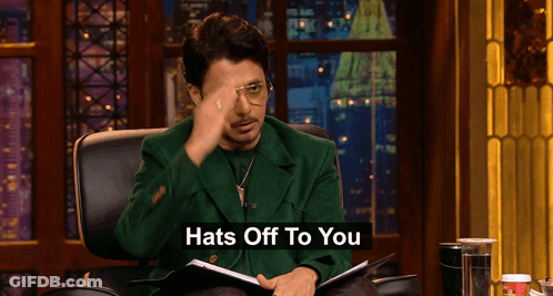 Man In Green Jacket Sitting With Hats Off Sign GIF