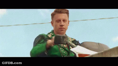 Man In Green Jacket Standing On Roof Holding Cup GIF