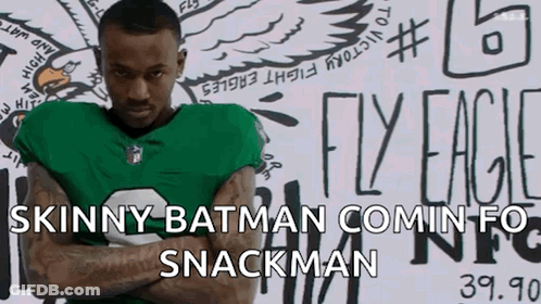 Man In Green Jersey With Arms Crossed In Front Of Skinny Batman Comin Fo Snackman Sign GIF