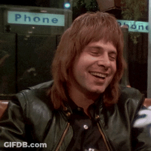 Man In Green Leather Jacket Smiling In Front Of Phone Booth GIF
