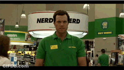 Man In Green Nerd Shirt In Front Of Sign Saying Buy More GIF