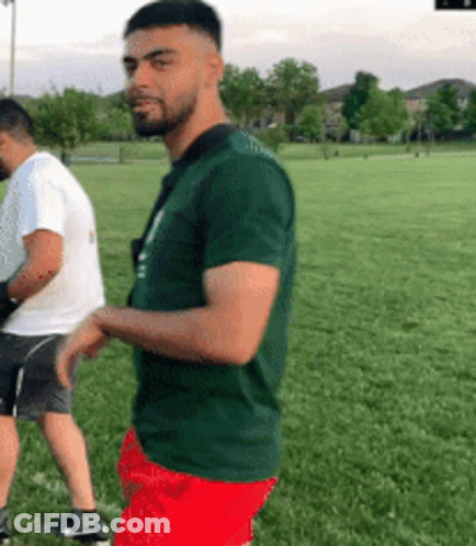 Man In Green Shirt And Red Shorts Next To Man In White Shirt GIF