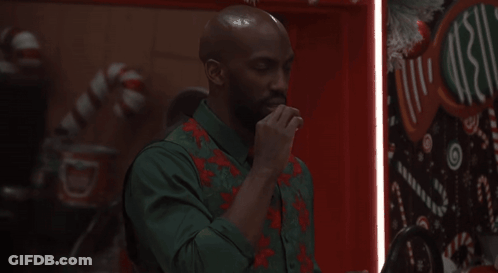 Man In Green Shirt And Red Vest In Front Of Christmas Sign GIF