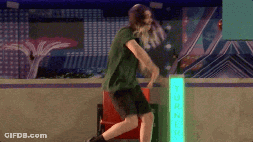 Man In Green Shirt Dancing In Front Of Turner Neon Sign GIF