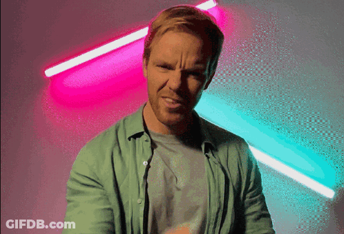 Man In Green Shirt Making Funny Face In Front Of Neon Lights GIF