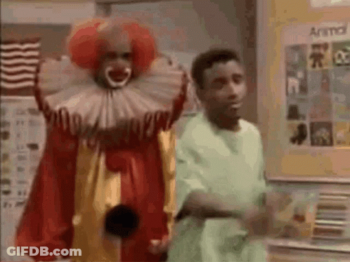 Man In Green Shirt Next To Clown In Red And Yellow Costume GIF