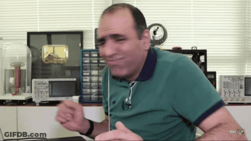 Man In Green Shirt Sitting At Desk With Clock GIF