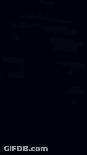 Man In Green Shirt Sitting On Ground Looking At Phone And Smiling GIF