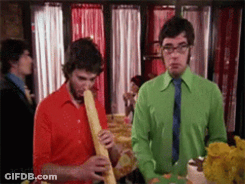 Man In Green Shirt Smoking Cigarette Next To Man In Red Shirt GIF