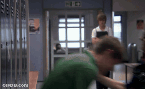 Man In Green Shirt Standing In Front Of Lockers With Fire Exit Sign GIF