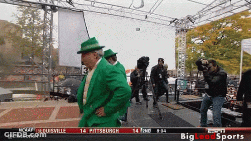 Man In Green Suit And Hat In Front Of NCAAF Sign GIF