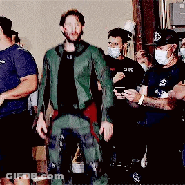 Man In Green Suit Standing Before Masked Group GIF