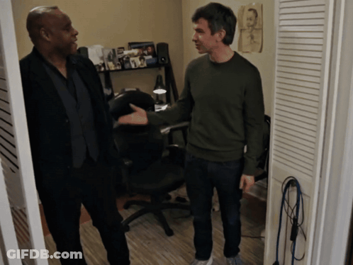 Man In Green Sweater Talking To Another Man In Dark Room GIF