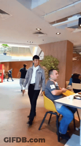 Man In Grey Jacket Walking Past Man With Number 18 Shirt GIF