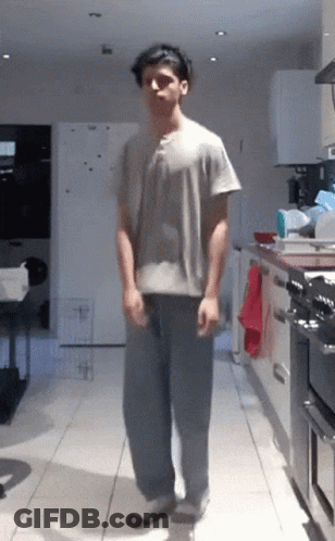 Man In Grey Shirt And Blue Pants Standing In Kitchen GIF