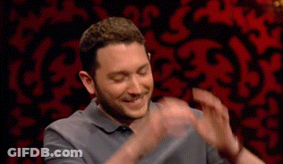 Man In Grey Shirt Clapping In Front Of Red Wall GIF