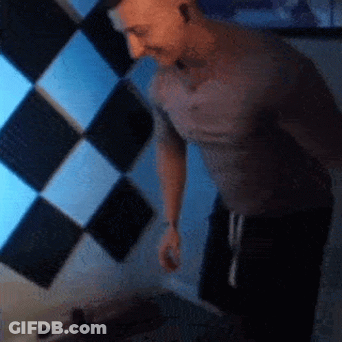 Man In Grey Shirt In Front Of Checkered Wall GIF