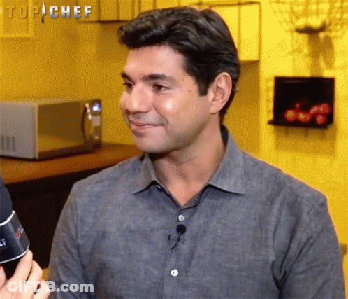Man In Grey Shirt Smiling In Front Of Microwave Top Chef Sign GIF