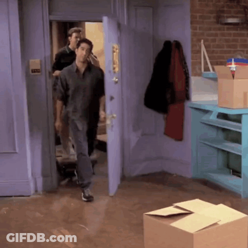 Man In Grey Shirt Walking Into Room With Boxes GIF